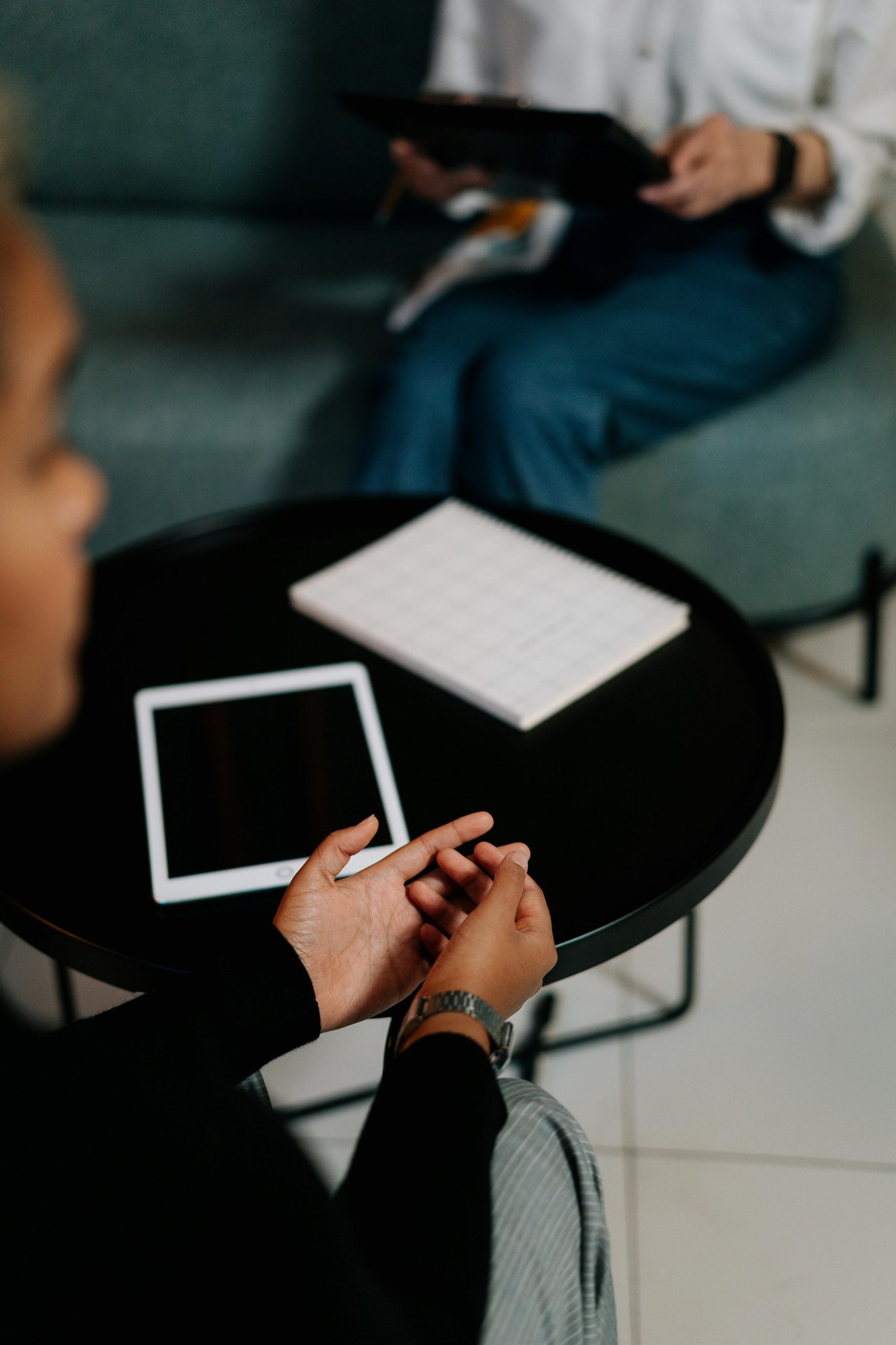 Two professionals discussing work in an office. Tablets and a notebook on the table.